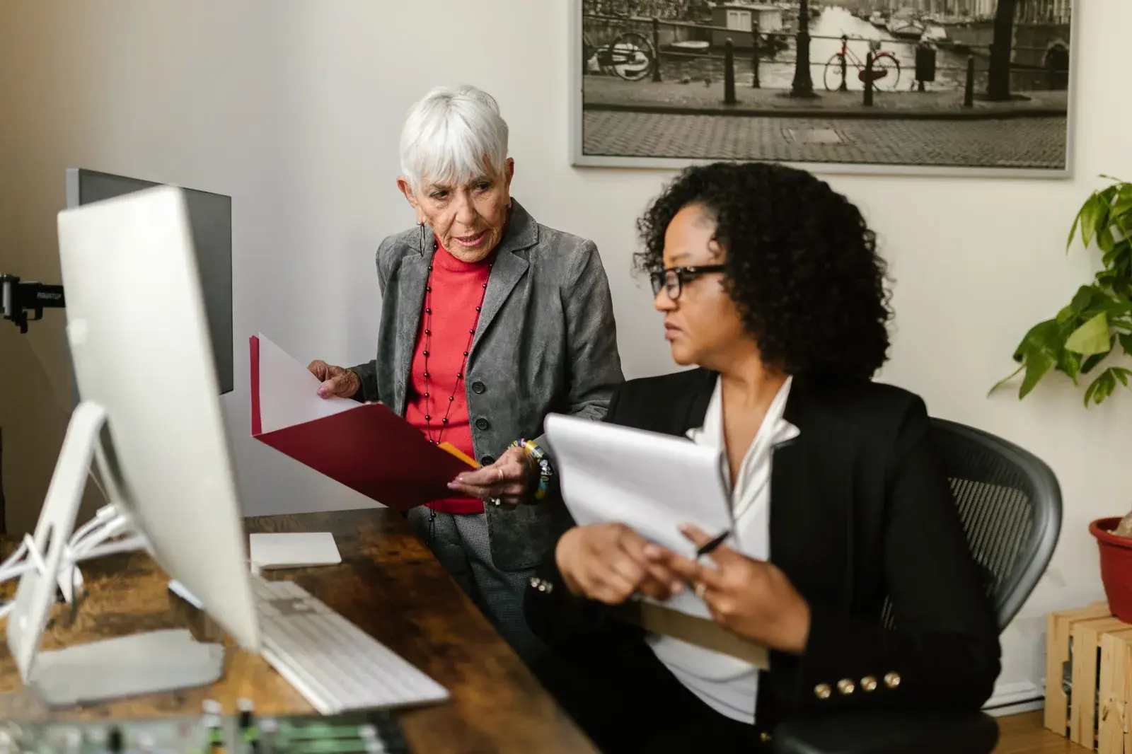 Two professionals at a desk reviewing papers, one holding an open red folder