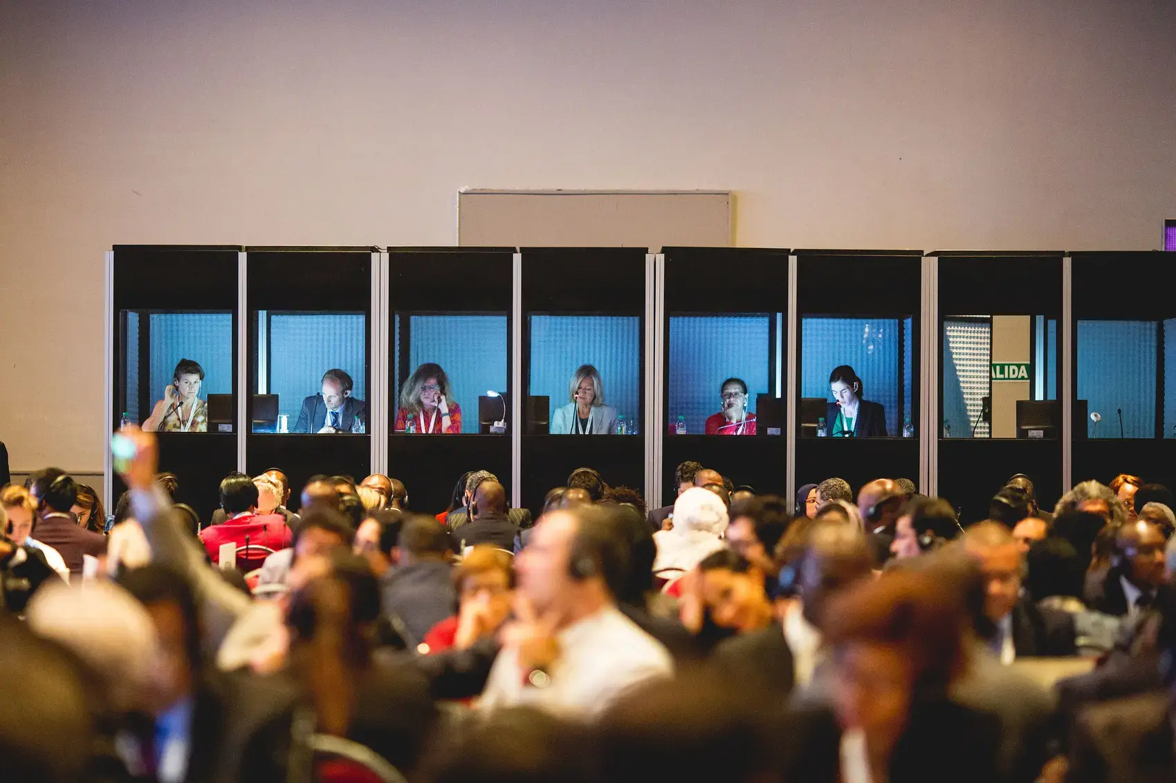 Interpreters in glass booths above a crowded international delegation meeting